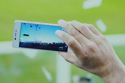 Cropped hand photographing stadium through smart phone