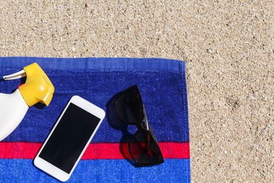 High angle view of mobile phone with sunglasses and spray bottle on towel