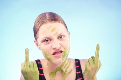 Close-up portrait of young woman showing obscene gesture against blue background