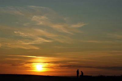 Silhouette people on land against sky during sunset