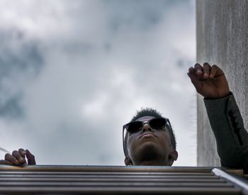 Low angle view of man wearing sunglasses against cloudy sky