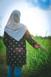 Rear view of woman standing on field against sky