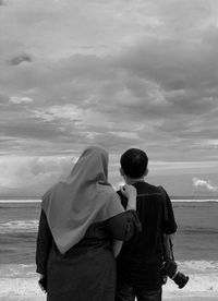 Rear view of couple on beach against sky