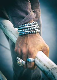 Cropped image of man wearing rings and bracelets holding railing