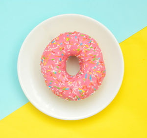 Pink glazes donut on white plate on pastel yellow turquoise background. sweet dessert.