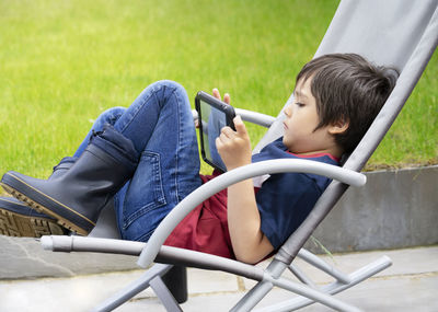 Rear view of boy using mobile phone while sitting on grass