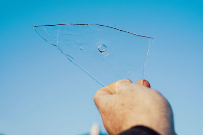 Close-up of hand holding ice against blue sky