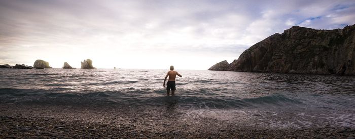 Man standing on rock by sea against sky