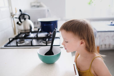 Cute toddler child in kitchen by stove helps mom cook, bright interior of kitchen