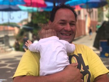 Close-up portrait of smiling father carrying baby outdoors