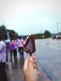 Cropped hand holding ice cream against sky
