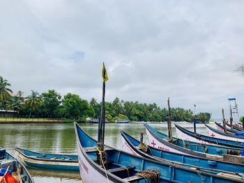 Boats moored in river against cloudy sky