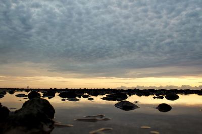 Rocks on beach against sky during sunset