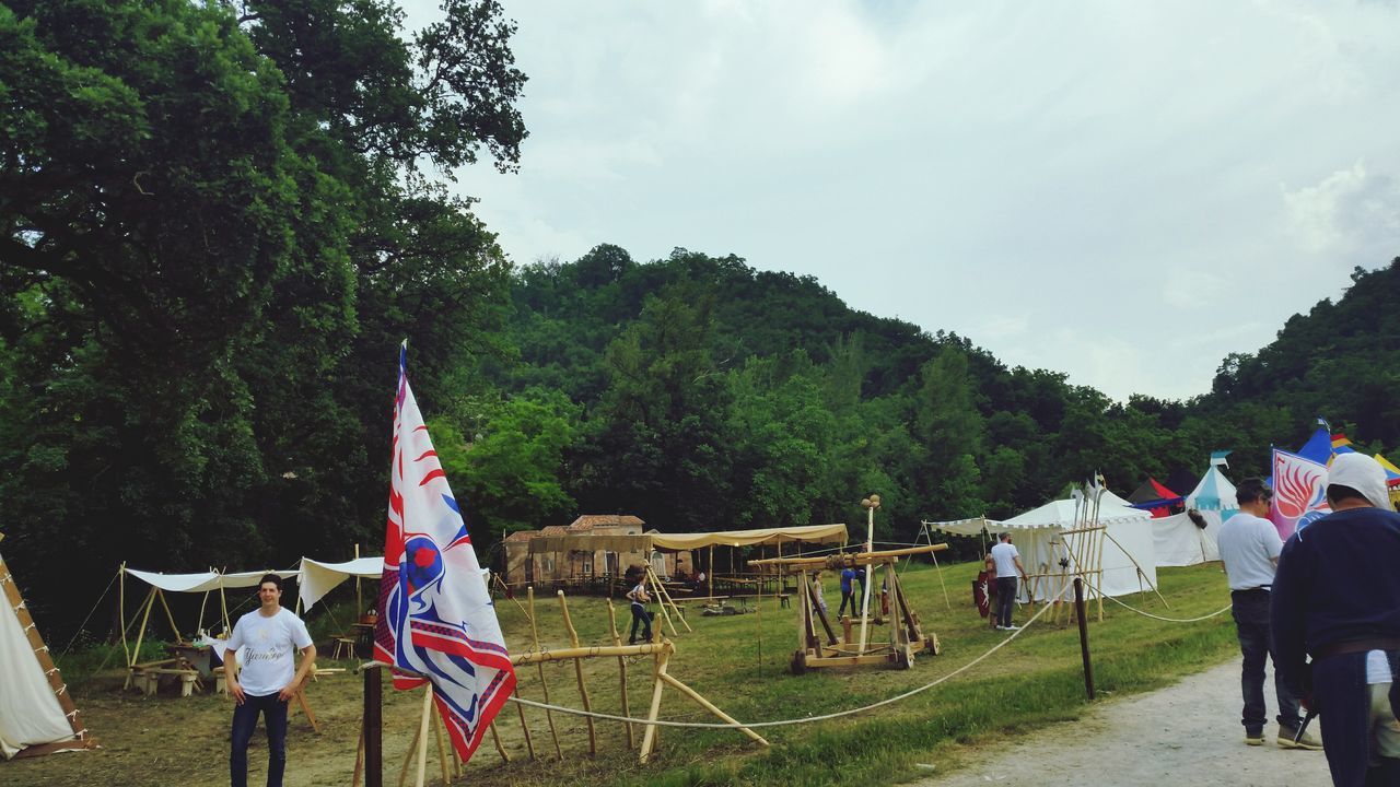 men, tree, lifestyles, person, leisure activity, large group of people, sky, grass, casual clothing, rear view, flag, walking, standing, patriotism, day, outdoors, park - man made space, umbrella, field