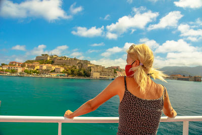 Woman standing by railing against sea against sky