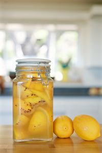 Pickles in glass jar by lemons on table at home