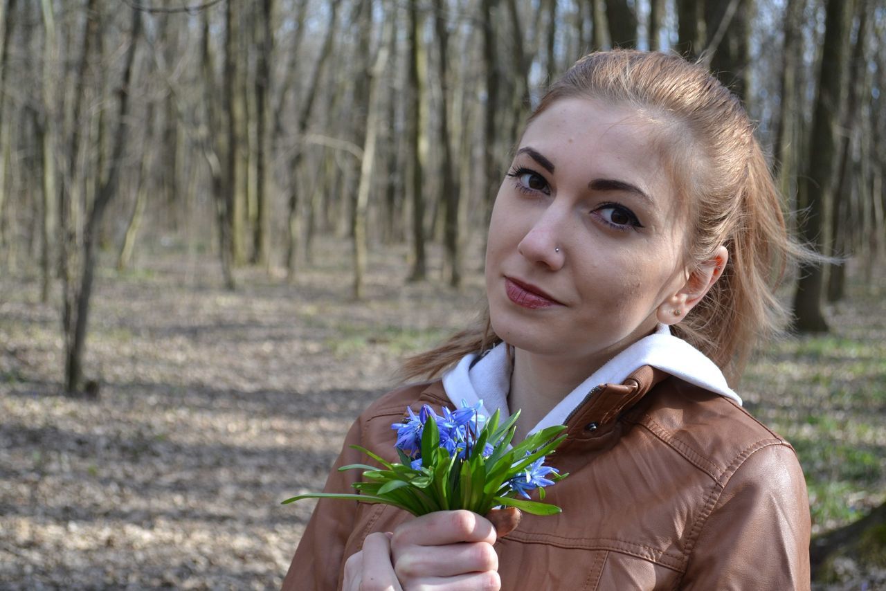 lifestyles, focus on foreground, person, leisure activity, young adult, flower, casual clothing, headshot, front view, portrait, tree, young women, waist up, looking at camera, holding, smiling, standing, growth