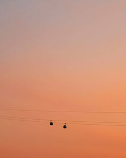 Low angle view of silhouette overhead cable cars against orange sky during sunset