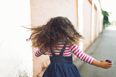 Rear view of girl running by wall on street