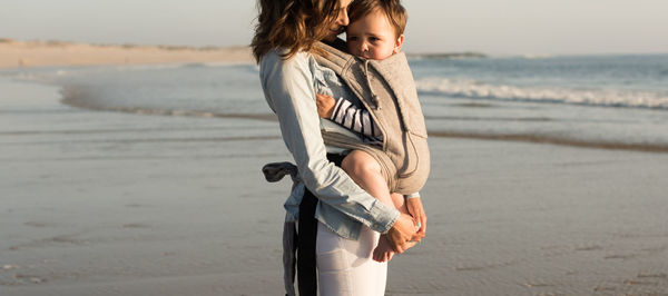 Mother carrying son while standing at beach