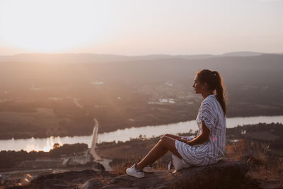 Woman sitting on mountain against sky during sunset