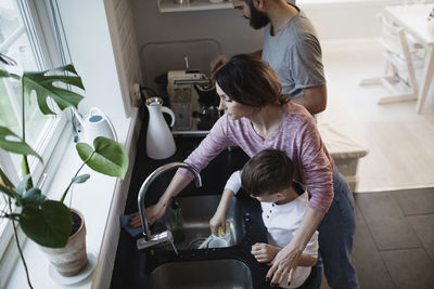 High angle view of man standing by woman cleaning counter while boy washing dishes in kitchen