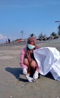 Portrait of woman cleaning beach while crouching on beach 