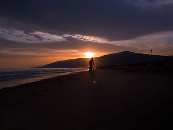 Silhouette people on beach against sky during sunset