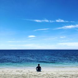 Rear view of man sitting on beach against sky