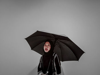 Woman holding umbrella while standing against white background