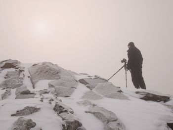Photographer takes picture of freeze snowy mountains rocks. extreme misty weather. stony rock peak 