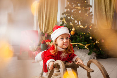 Cute girl lying down on sledge against christmas tree