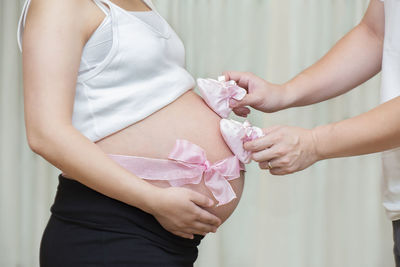 Cropped hands holding baby booties on pregnant woman belly at home