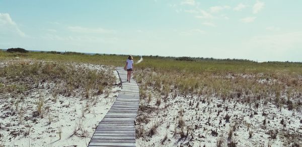 Rear view of girl walking on boardwalk against sky