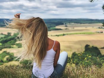 Rear view of woman with long hair looking at landscape while sitting on field