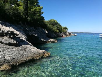 Scenic view of sea and rocks against clear blue sky