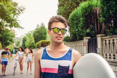 Young man wearing sunglasses with friends in background on road