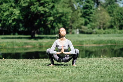 Full length of woman exercising on field by lake at park