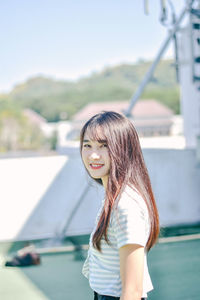 Portrait of young woman smiling while standing against retaining wall