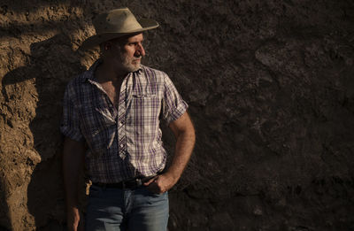 Portrait of adult man in cowboy hat and shirt against abandoned building