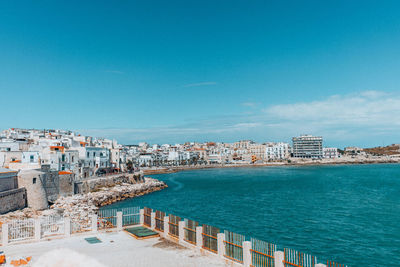 Buildings by sea against blue sky