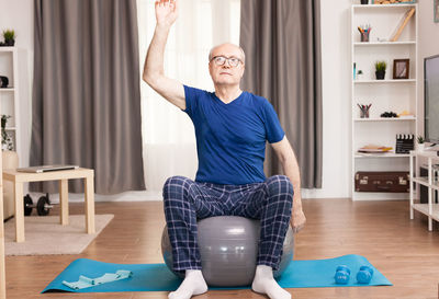 Man with hand raised sitting on fitness ball at home