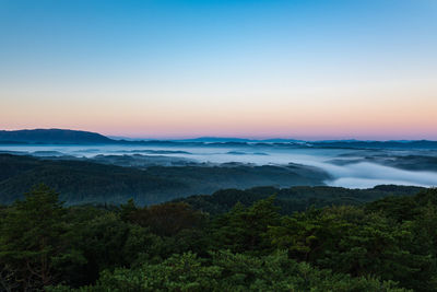 Scenic view of landscape in foggy weather against blue sky