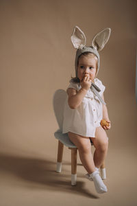 Toddler baby girl in funny hat with ears sitting with eggs in her hand