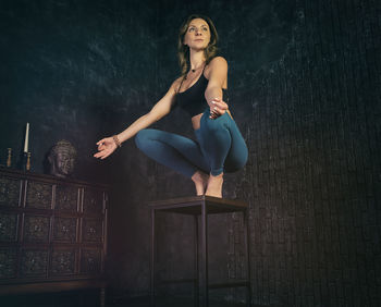 A charming girl in a sports uniform does yoga in an old room with a fireplace and candles