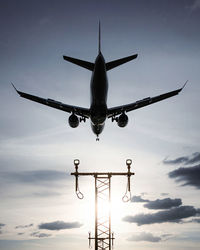 Low angle view of airplane flying past approach lights against sky during landing 