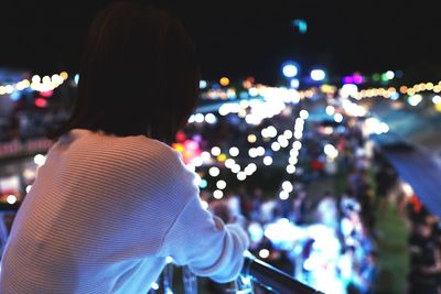 Rear view of woman standing against illuminated city at night
