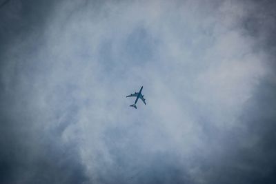 Low angle view of airplane flying against cloudy sky