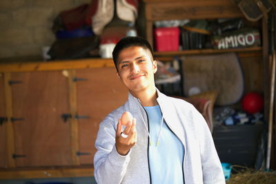 Portrait of a smiling young man hoding an egg in a stable