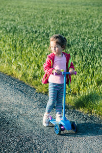 Cute girl with push scooter standing on road